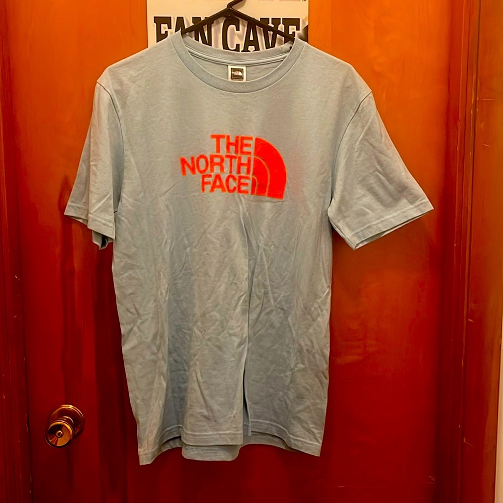 The North Face, shirt color: blue w/ orange lettering. Shirt size: medium